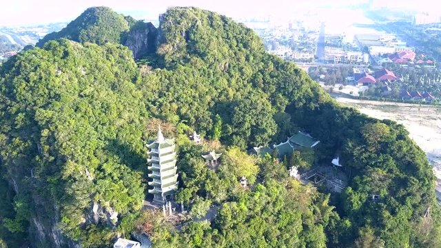 fantastic aerial picture camera lowers from forestry hill top to temple pagoda among trees against modern city
