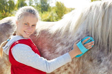Girl grooming horse  in the outdoors.