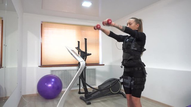 Beautiful athletic brunette doing EMS exercises with dumbbells. Hand exercises