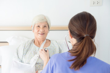 Obraz premium Happy asian senior patient lying in bed and smiling at camera while doctor exam by stethoscope