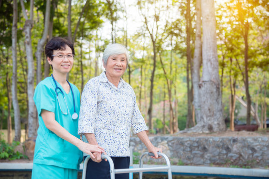 Disabled senior asian woman walking with assistance from nurse in hospital park