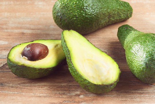 Closeup photo of avocado cut to half, brown seeds visible, with more avocados on brown wooden background – Image