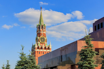 Fototapeta na wymiar Spasskaya tower of Moscow Kremlin on a background of Lenin's Mausoleum against blue sky with white clouds at sunny day