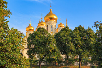 Fototapeta na wymiar Cathedral of the Annunciation on Moscow Kremlin territory against blue sky and green trees in sunny early morning