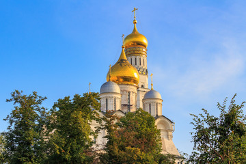 Fototapeta na wymiar Cathedral of the Archangel and Ivan the Great Bell-Tower on Moscow Kremlin territory on a blue sky and green trees background in sunny morning