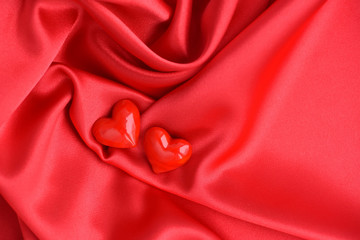 Two glass hearts on red satin fabric background