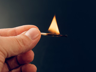 Match with a fire flame burning being held by a hand