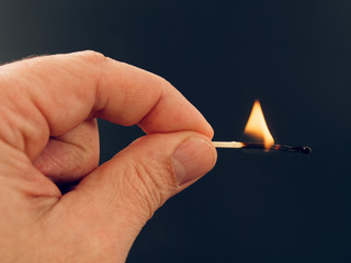 Match with a fire flame burning being held by a hand