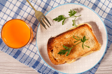 Toast with butter and cheese on white plate and glass of orange juice.