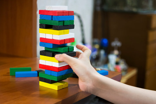 The Hand Dismantles The Tower Of Multicolored Wooden Bars. Concept: Children's Leisure, Board Games, Instability, Precarious Situation.