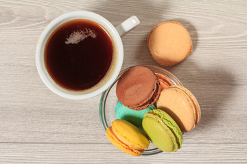 Cup of coffee and delicious macarons cakes of different color in glass bowl.