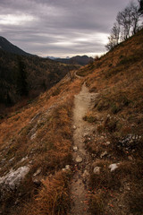 Kleiner Wanderpfad führt in weite Berglandschaft unter bewölktem Himmel