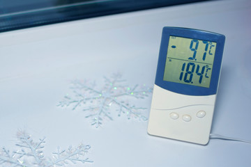 Electronic thermometer is on the windowsill and shows the temperature in Celsius on the street and...