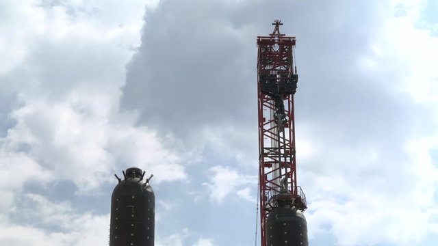 Heat haze. Air cooler for oil refinery. Industrial, Oil refinery. Tower crane lifts a huge metal pipe. The worker controls the installation of the equipment on the construction site.