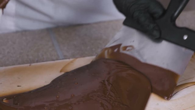 Tempering melted chocolate on natural stone. Woman's hands and spatula close-up.
