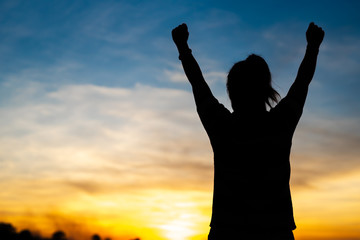 Fototapeta premium A happy young woman looks up at success and at sunset.