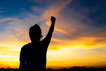 A happy young woman looks up at success and at sunset.