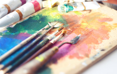 Obraz premium The artist's workplace: palette, brushes, tubes of oil paint and palette knife. Everything is illuminated by the sun.