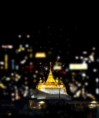 Wat Saket, Golden Mount temple on dark night, with blurred light bokeh of city.