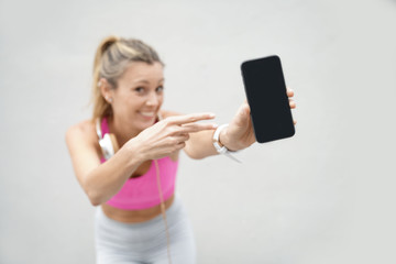 Fototapeta premium Smiling woman in sporstwear pointing to cellphone on white background