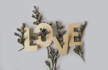 “LOVE” Wooden letters , decorated with purple Statice flowers on a white background.