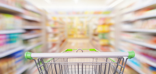 Supermarket aisle interior shelves blur background with empty green shopping cart