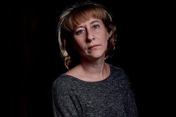 Portrait of a sad middle-aged woman in the room. Photo shoot in a dark key