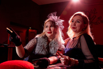 Two fat women with playing cards in a dark room with red light. Gangsters style