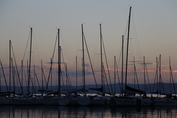 A warm, pleasant summer evening at Lake Balaton. Yachts, sailboats, boats with masts in the marina, port. Mountains visible in the background. A beautiful twilight. Orange sky. A quiet end of the day.