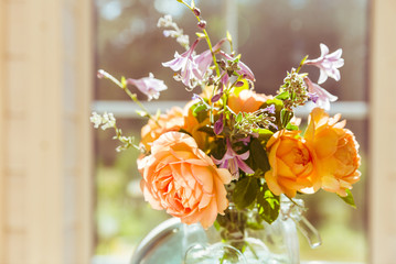 Valentine's Day, orange English rose flowers in a glass jar on the background of a large window of a wooden house, space for text, vintage style, retro interior with flowers.