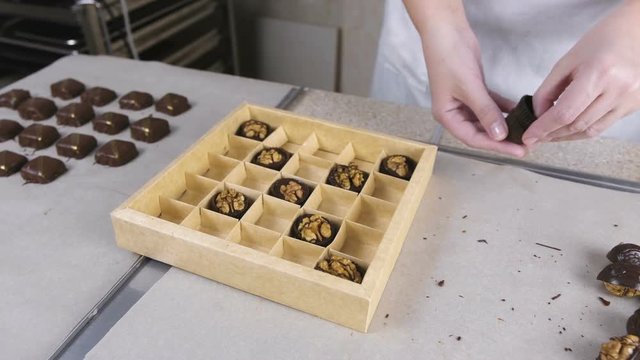 Baker's hands put handmade chocolate candies in a beautiful box. Present box of chocolate sweets.