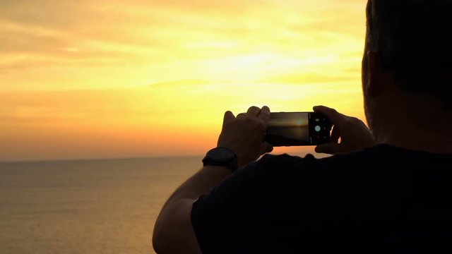 Close up on man's hands taking a photo with cell phone of beautiful sunset over the sea