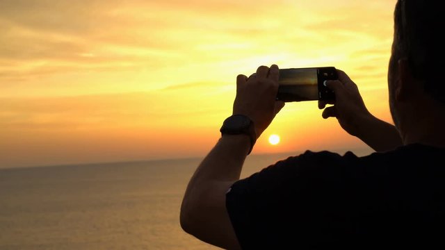 Close up on man's hands taking a photo with cell phone of beautiful sunset over the sea