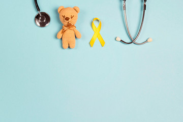 Childhood Cancer Awareness Yellow Ribbon with toy bear and stethoscope on blue background with copy...