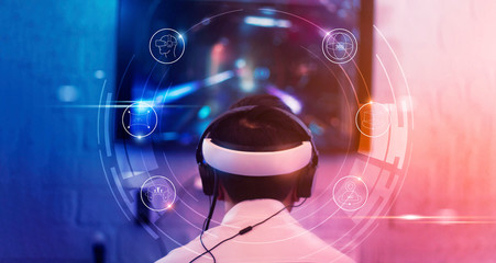Young gamer wearing VR goggles and headset with icon VR playing and winning driver and shooter online video game on his personal computer in the room lit by neon lights, eSport network online. © ipopba