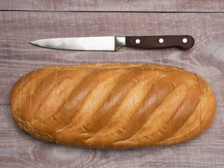 Sliced loaf of white bread and knife on a brown wooden background