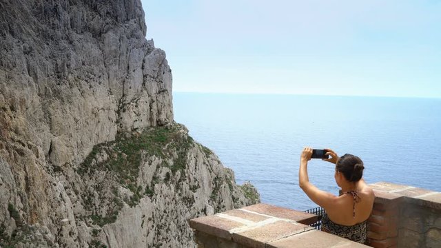 Young tourist woman taking picture of beautiful view over the sea , Sardinia, Italy