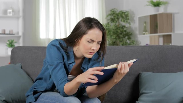 Tired woman suffering eyestrain reading a paper book sitting on a couch at home