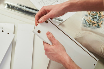The furniture assembler joins together the two parts of the ready-to-assemble furniture with cam lock connections and wooden dowel pin, flat pack furniture assembly service, snap-together joints