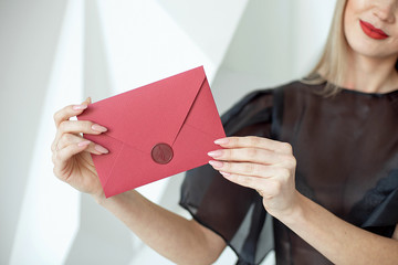 Close-up woman with slim body holding invitation envelope card in hands, rear veaw.