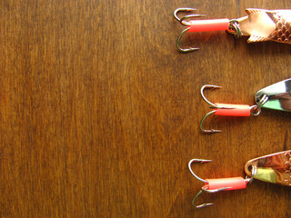 Three shiny artifician baits: details of fishing spinners upright on a wooden dark background with...