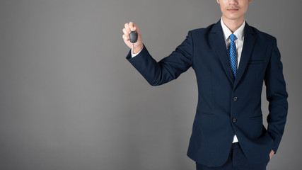 Business man is holding car key, grey background in studio