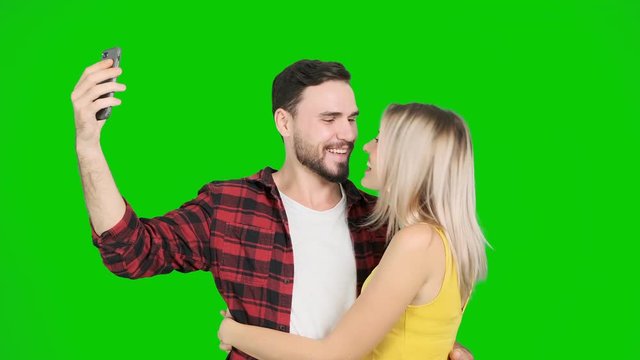 Young man taking selfie with woman on green screen and kiss. White male and female, chroma key.