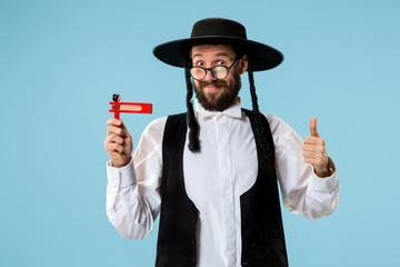 Portrait of a young orthodox Hasdim Jewish man with wooden Grager Ratchet at Jewish festival of...