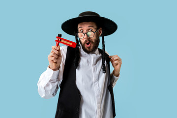 Portrait of a young orthodox Hasdim Jewish man with wooden Grager Ratchet at Jewish festival of Purim at studio. The purim, jewish, festival, holiday, celebration, judaism, pastry, tradition, cookie