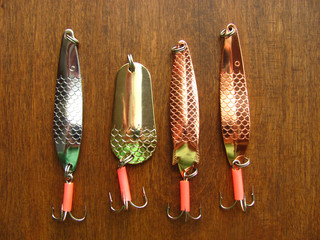 Four shiny artifician baits: fishing spinners is on a wooden dark background. Close up top view....