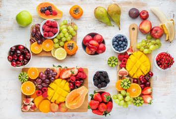 Healthy breakfast, cut colorful rainbow fruits, strawberries raspberries oranges plums apples kiwis grapes blueberries mango persimmon, copy space, selective focus