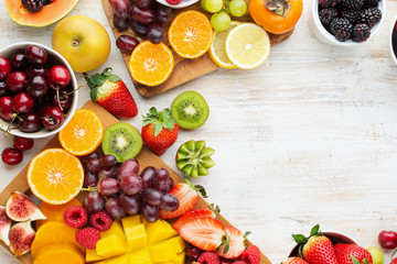 Healthy raw fruits background, cut mango, strawberries raspberries oranges plums apples kiwis grapes blueberries cherries, on white table, copy space, top view, selective focus