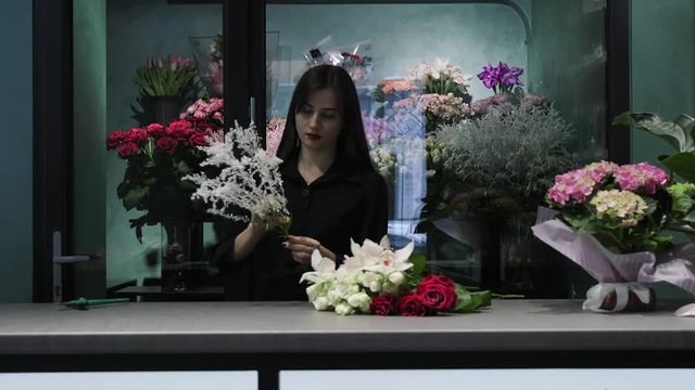 Professional woman florist prepare solidago for the bouquet with roses and orchids in floower shop.