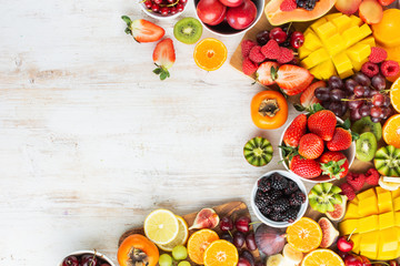 Healthy raw fruits background, cut mango, strawberries raspberries oranges plums apples kiwis grapes blueberries cherries, on white table, copy space, top view, selective focus